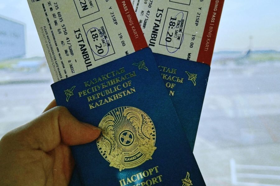 A Kazakhstan passport holds two airline tickets against an airport backdrop in Warsaw, Poland.